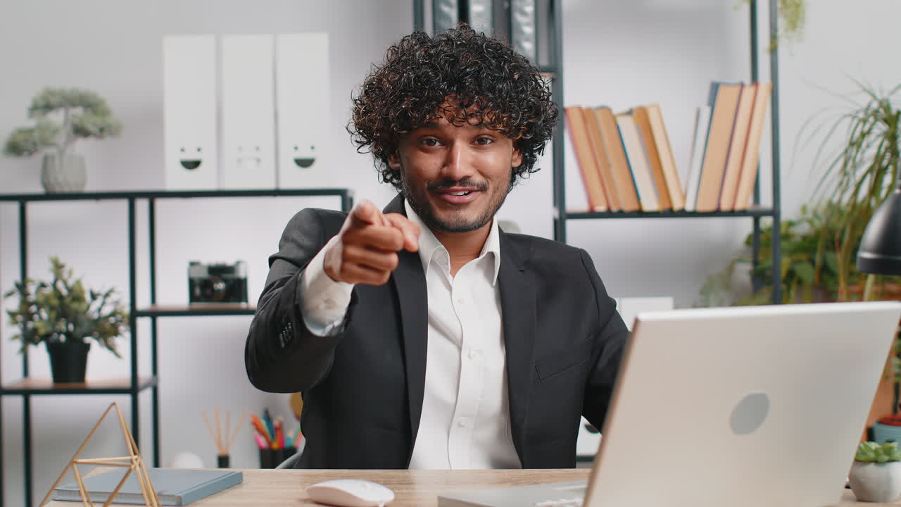 Business man working on office laptop pointing to camera looking with happy expression making choice