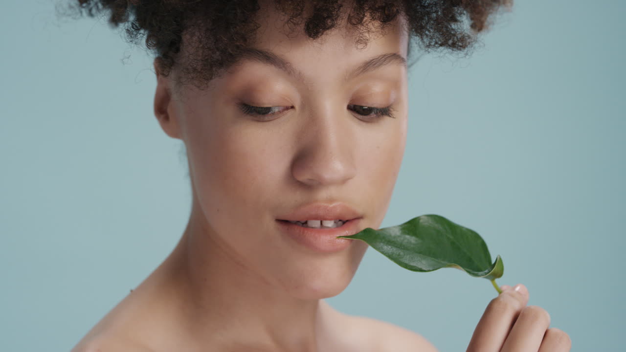retrato de cerca mujer joven sexy tocando la cara con hojas acariciando suave tez saludable disfrutando de la belleza natural juguetona sobre fondo azul concepto de cuidado de la piel