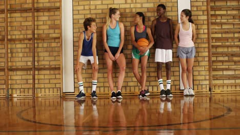 niños de secundaria apoyados contra la pared en la cancha de baloncesto