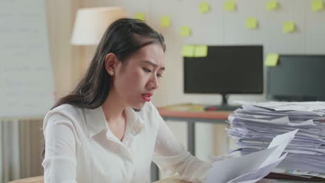 close up of tired asian woman yawning while working hard with documents at the office
