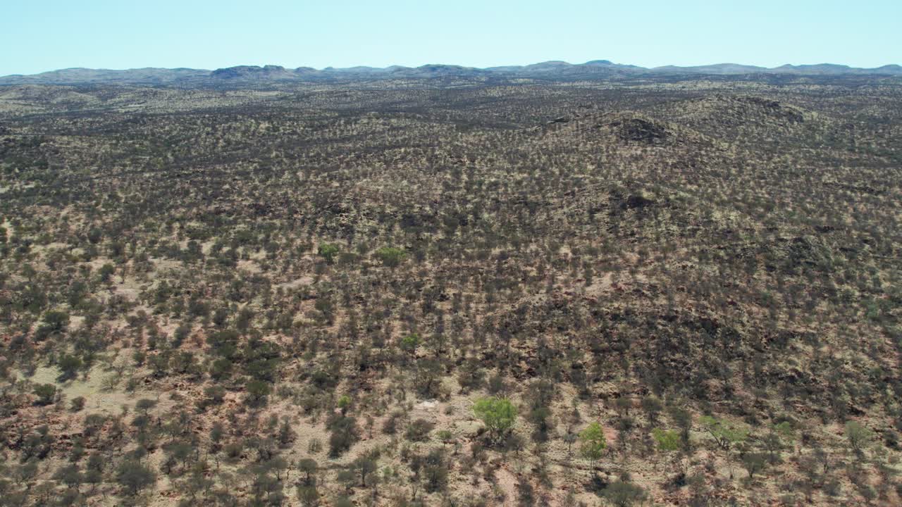 Reversing drone view of the dry rocky landscape north of Alice Springs, Mparntwe. Northern Territory, Australia. August 2022.