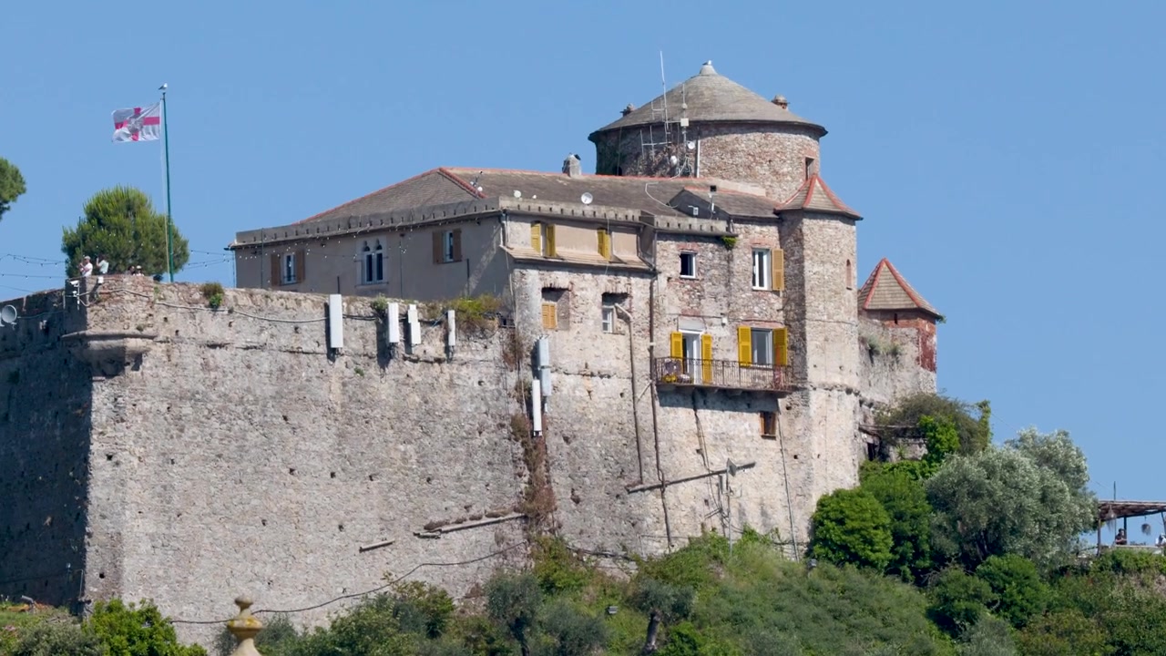 Un'ampia inquadratura di un castello storico in pietra su una collina verde sotto cieli azzurri.