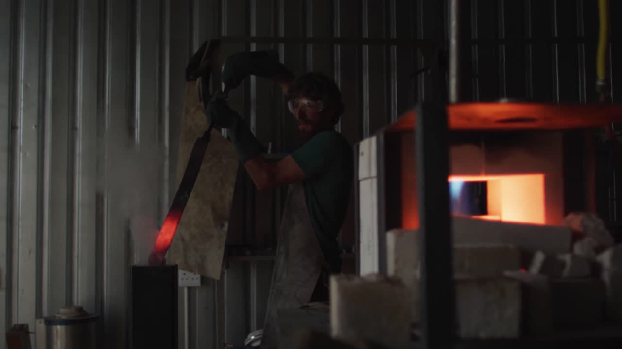hombre caucásico herrero calentando cuchilla de metal en el horno en el taller