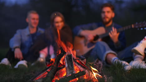 Friends playing guitar around campfire