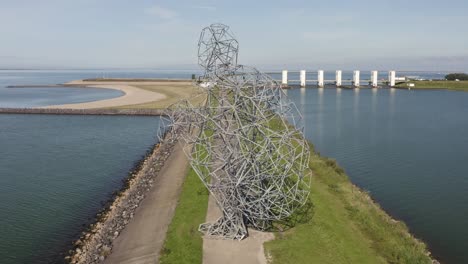 aerial shot of steel artwork on a dike with sluices in the background in lelystad, the netherlands, on a beautiful sunny summer day