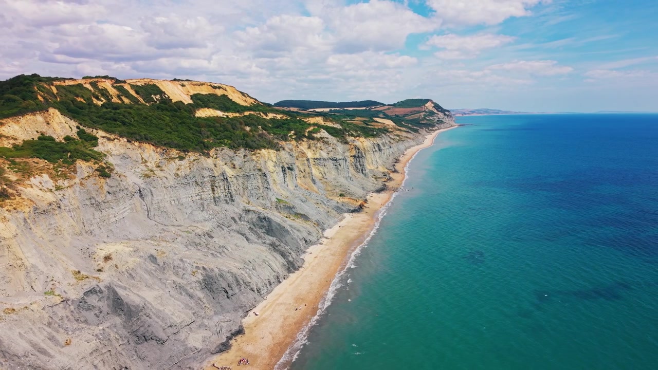 Splendide riprese aeree con drone che viaggiano accanto a scogliere ripide ed erose, una stretta spiaggia di ciottoli e un mare turchese e limpido vicino a Charmouth sulla Costa Giurassica del Dorset, Inghilterra. La vasta vista costiera.