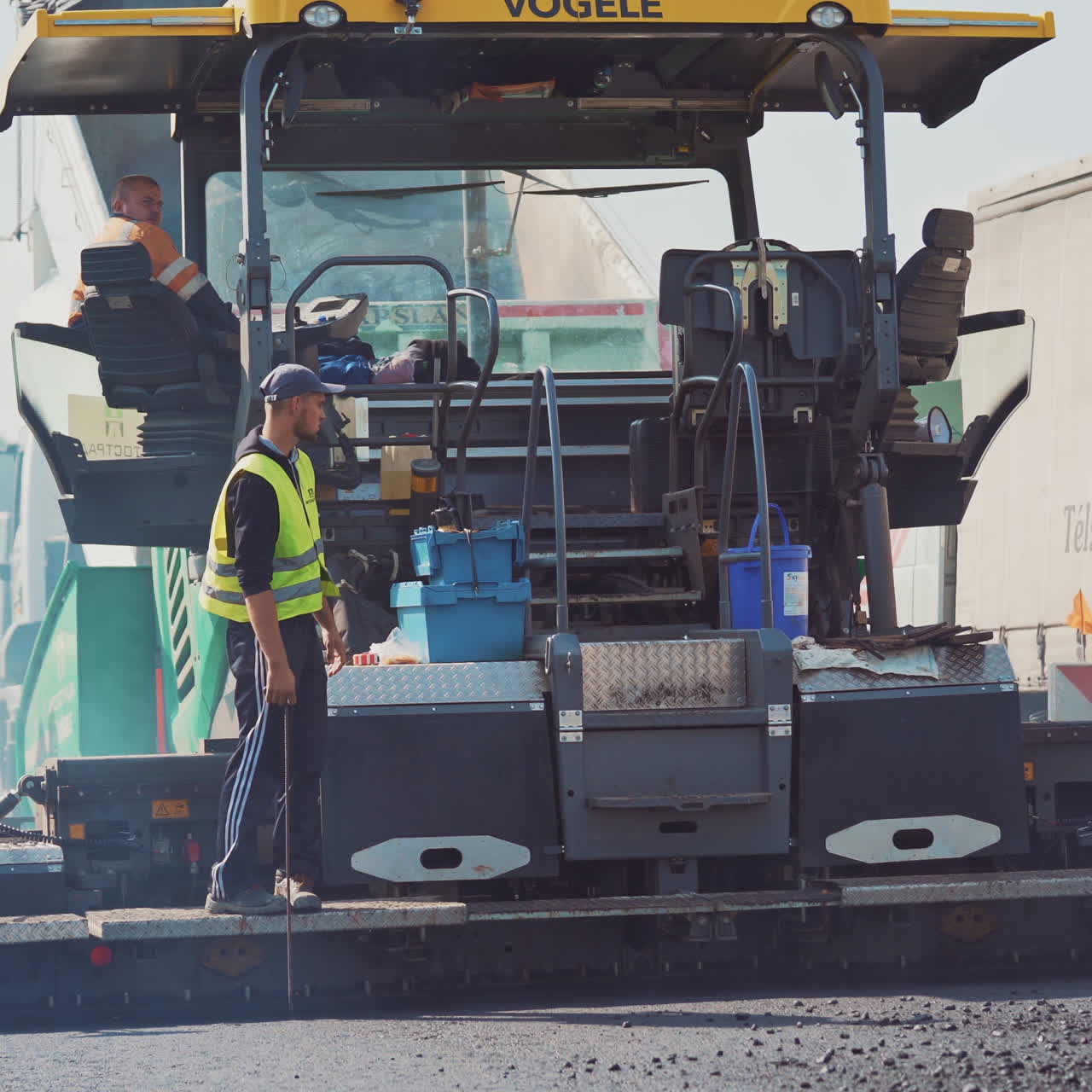 Process of lying new asphalt on the road. Group of workers in protective uniform working outdoors on the background of a big asphalt machinery.