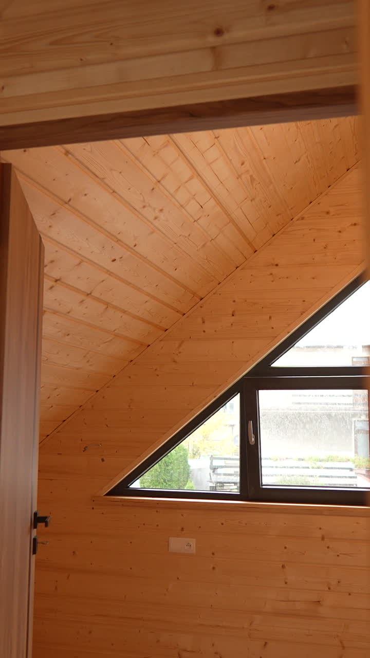 Un interno in legno presenta un soffitto inclinato e una finestra triangolare. Ideale per studi di architettura, presentazioni di interior design o progetti di ristrutturazione di case. Movimento fluido della camera con panning