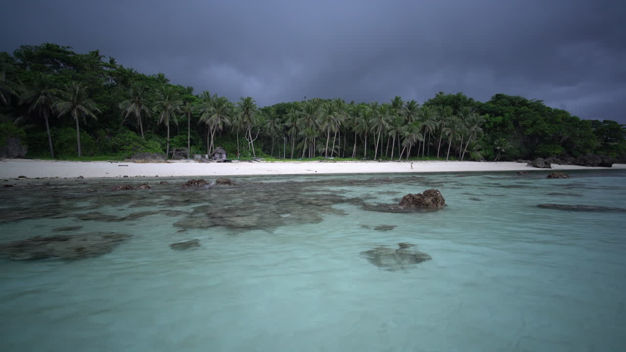 Vista de ángulo bajo desde aguas poco profundas mostrando playa de arena blanca y palmeras en la Isla Carabao cerca de Boracay, Filipinas, con mar tropical cristalino.