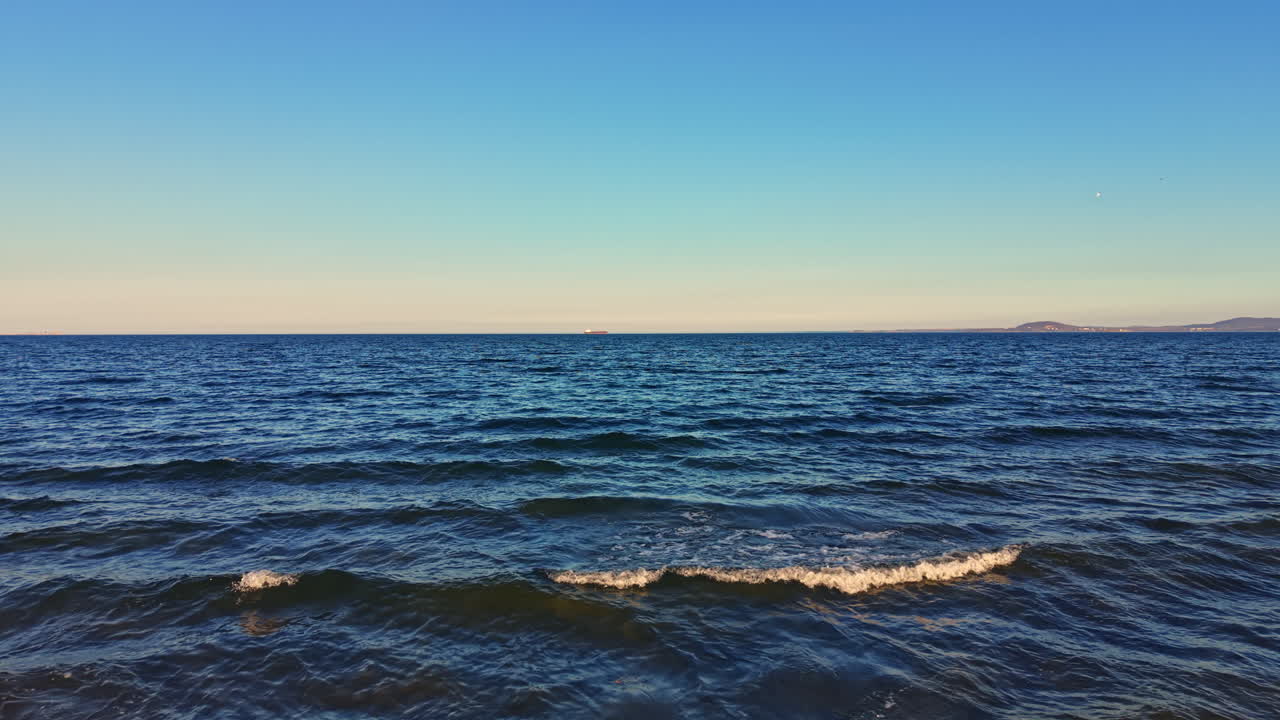 Blick auf das Meerwasser unter einem klaren blauen Himmel mit sanften Wellen, die sich tagsüber in Strandnähe dem Ufer nähern.