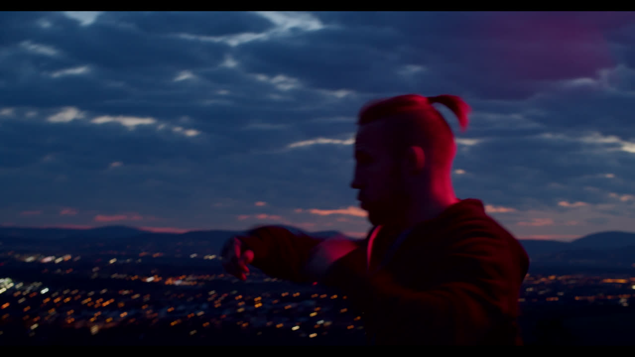 Man practicing martial arts at sunset over a city