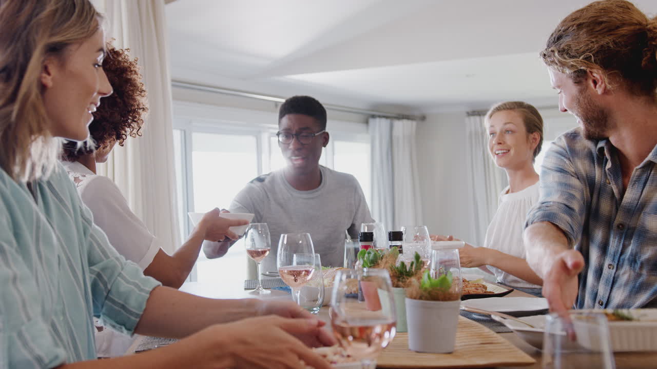 Gruppe unge venner sitter rundt et bord hjemme og hygger seg med et måltid sammen