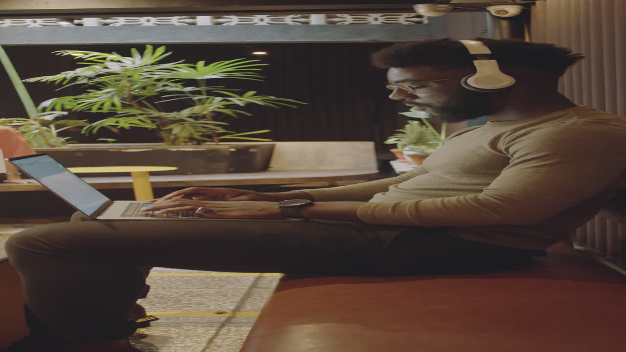 African American Man in Headphones Working on Laptop in Modern Cafe