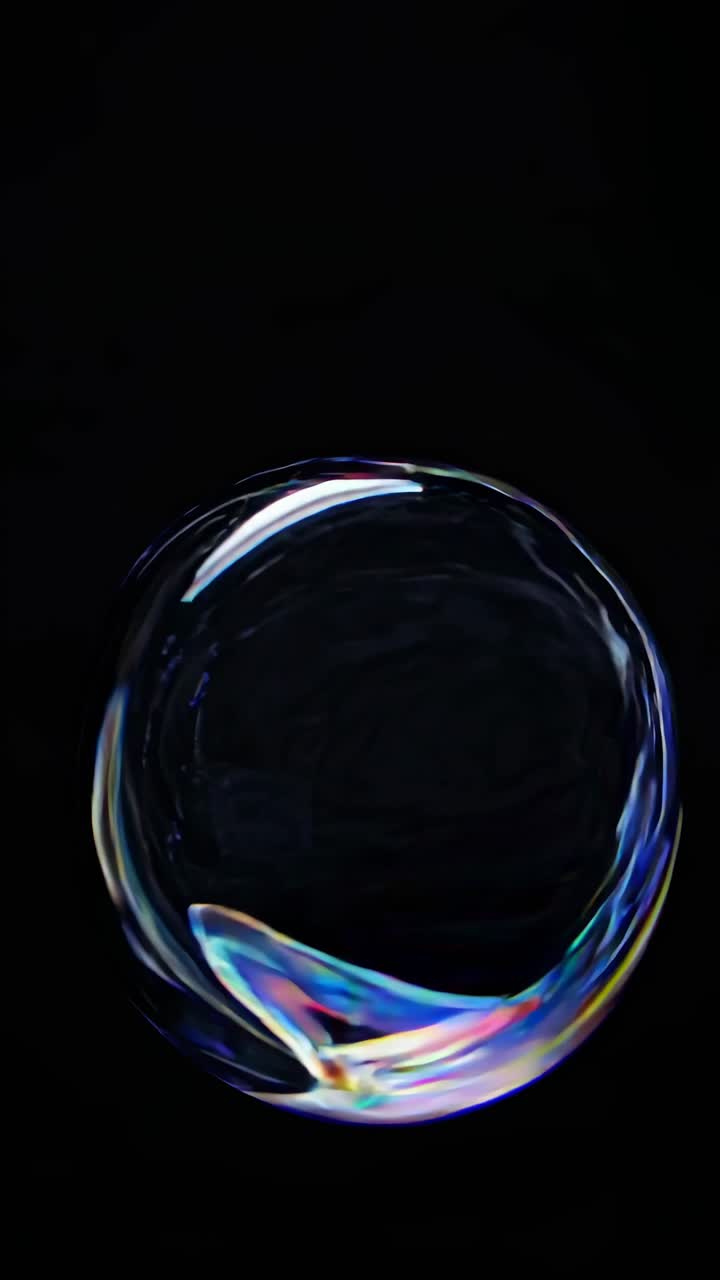 Close-up video of a soap bubble against a black background, capturing iridescent colors