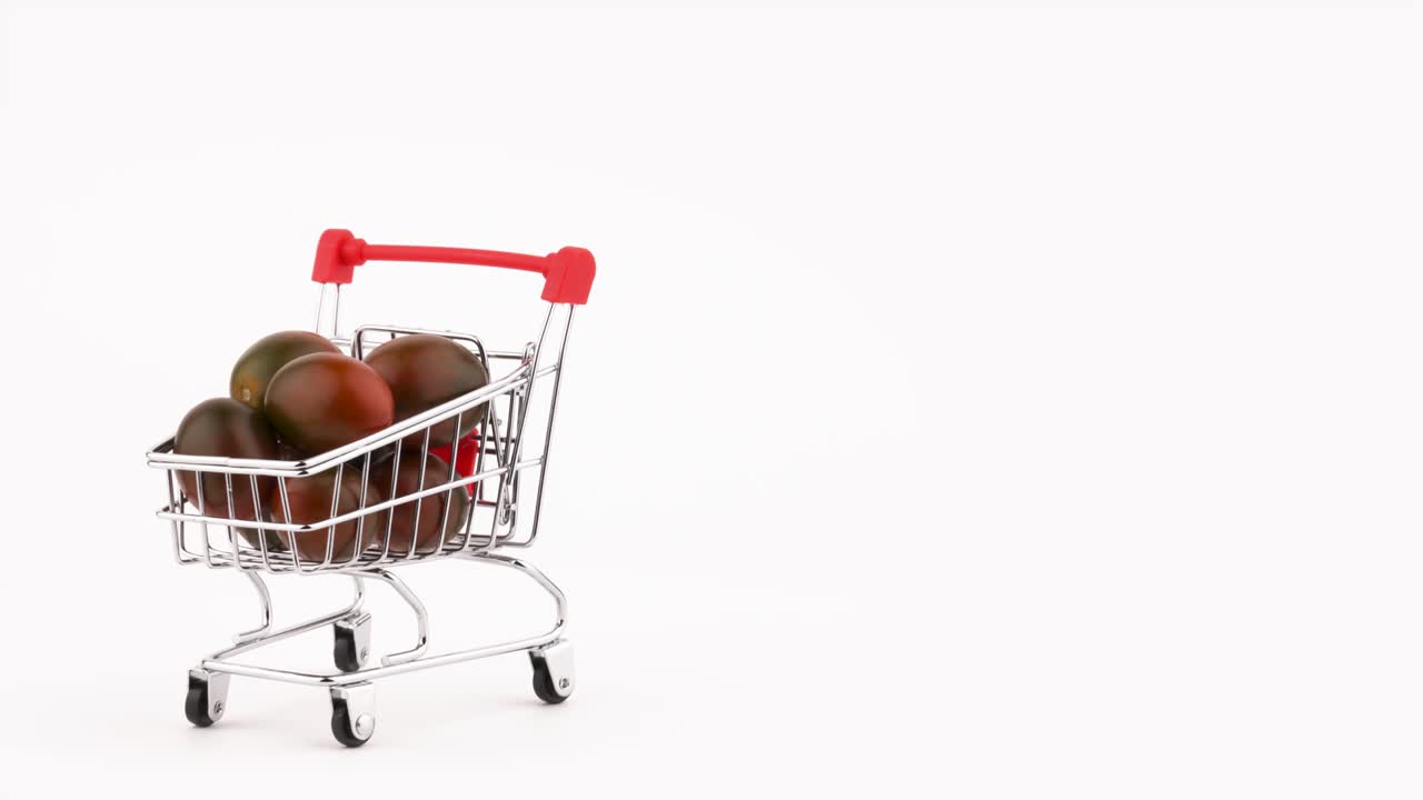 Pół klatki. Wózek na zakupy wypełniony stosem czarnych pomidorów winogronowych. Obracający się na obrotnicy. Izolowany na białym tle. Zbliżenie. Makro