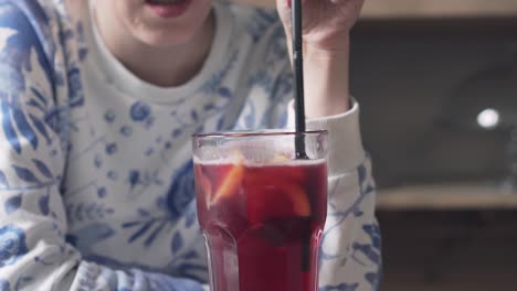 young girl is stirring a red lemonade in a glass with plastic straw