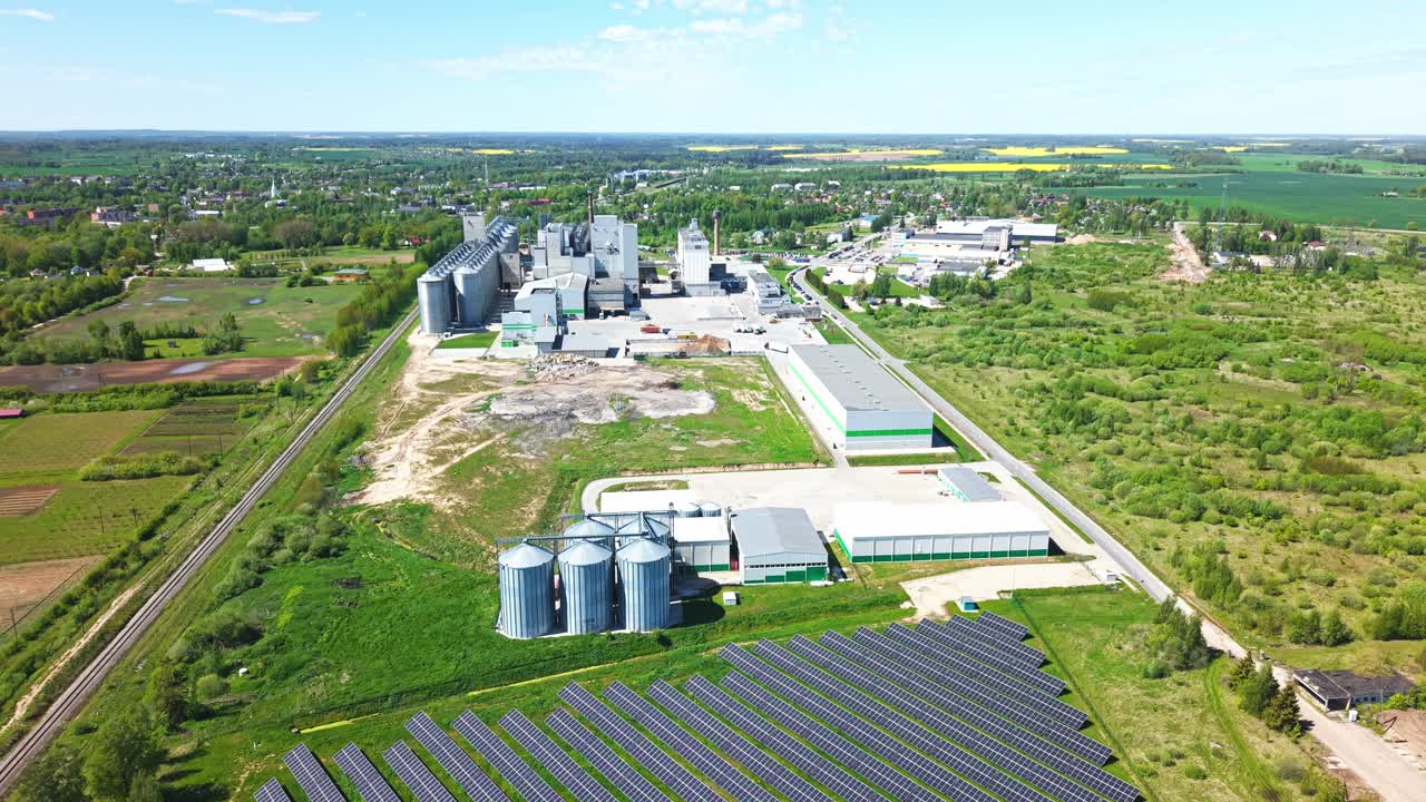 Solar panels in a field with silos and a factory building, aerial view