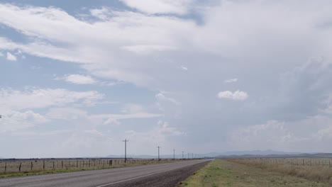 Wide-shot-of-empty-highway,-clouds-rolling-overhead-and-a-passing-train-in-the-distance