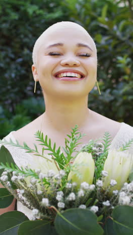 video vertical del retrato de una mujer biracial feliz con un ramo de flores en el jardín en un día soleado