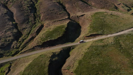 Drone-view-vehicle-driving-in-mossy-highlands-in-Iceland-countryside-speeding-offroad.--Aerial-view-4x4-car-driving-dust-road-desert-countryside-with-moss-hills.-Commercial-and-insurance