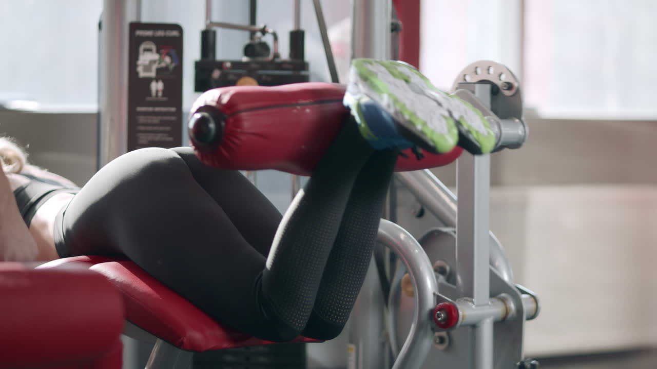 Fitness woman training leg flexion in sport simulator in gym.