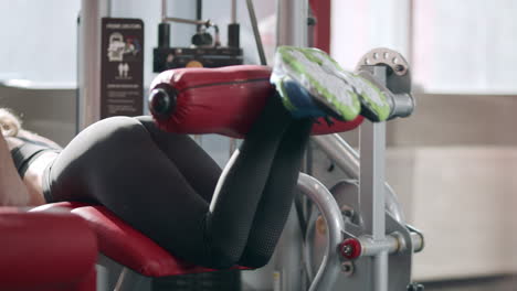 fitness woman training leg flexion in sport simulator in gym.