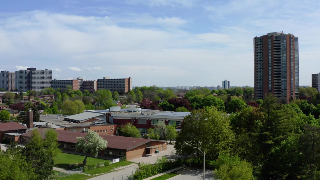 Lenta ripresa aerea con drone che domina un quartiere residenziale suburbano, caratterizzato da condomini a più piani, case unifamiliari, edifici comunitari, alberi verdi maturi e vegetazione lussureggiante