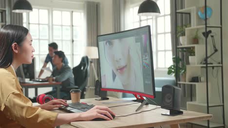 asian female digital editor works in photo editing software on her personal computer with big display in office