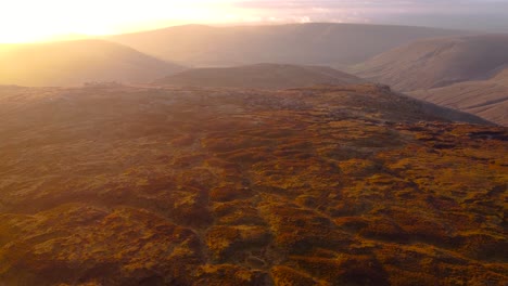 Vuelo-Cinematográfico-De-Drones-Sobre-El-Paisaje-De-Páramos-En-La-Cima-De-Las-Montañas-Kinder-Scout-En-El-Distrito-De-Los-Picos-En-Inglaterra---Rayos-De-Sol-En-El-Fondo-Durante-La-Puesta-De-Sol