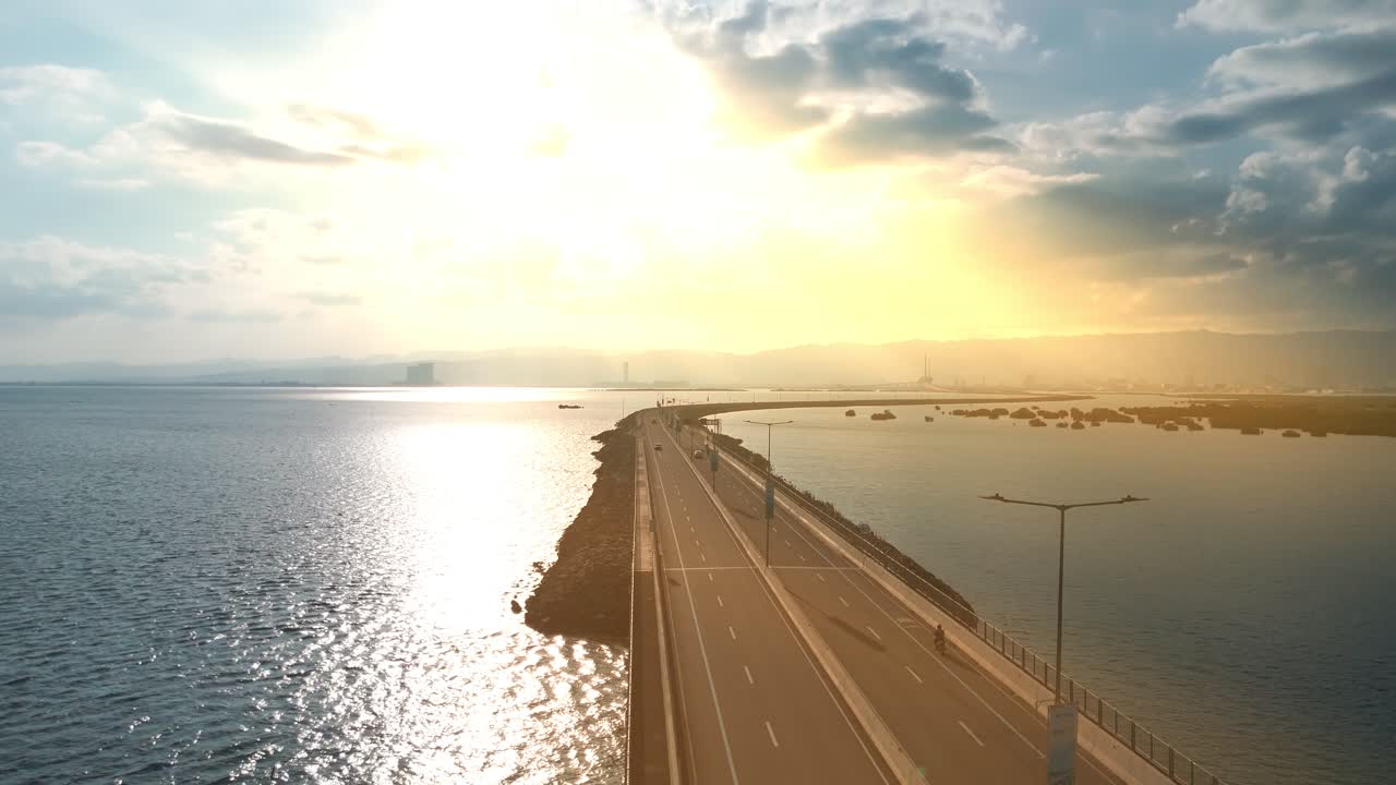Epic 4K drone shot of a bridge lit by sun rays breaking through clouds, with ocean, city skyline, and mountains in view. Ideal for cinematic edits
