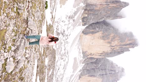 una mujer excursionista con impermeable rosa gira felizmente en la base de tre cime di lavaredo, italia