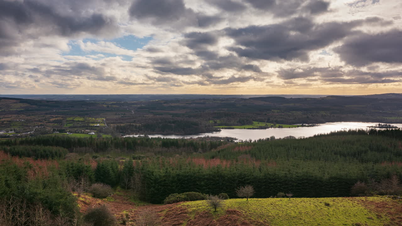 lapso de tiempo del paisaje agrícola rural con lago, bosque y colinas durante una puesta de sol nublada vista desde arriba lough meelagh en el condado de roscommon en irlanda