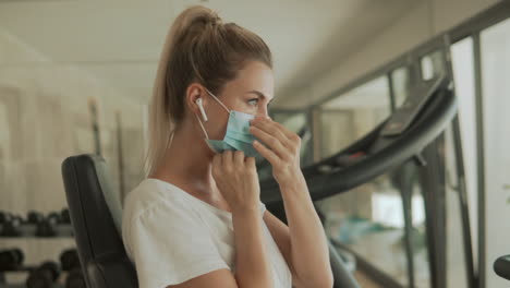 Young-athlete-female-puts-on-face-mask-and-looks-to-camera-in-the-gym.-Close-up.