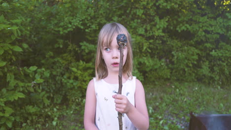 una niña linda mirando un malvavisco quemado en un palo