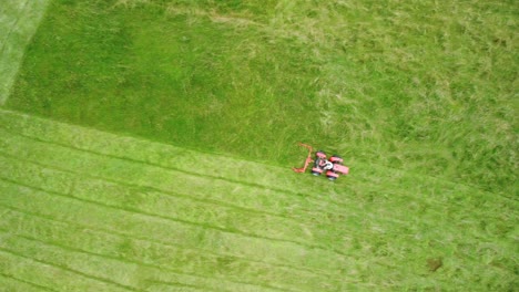 flying over red lawnmower tractor cutting straight lines of green grass