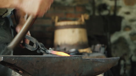 a blacksmith with forceps holds a red-hot billet above the anvil striking it with a hammer tradition