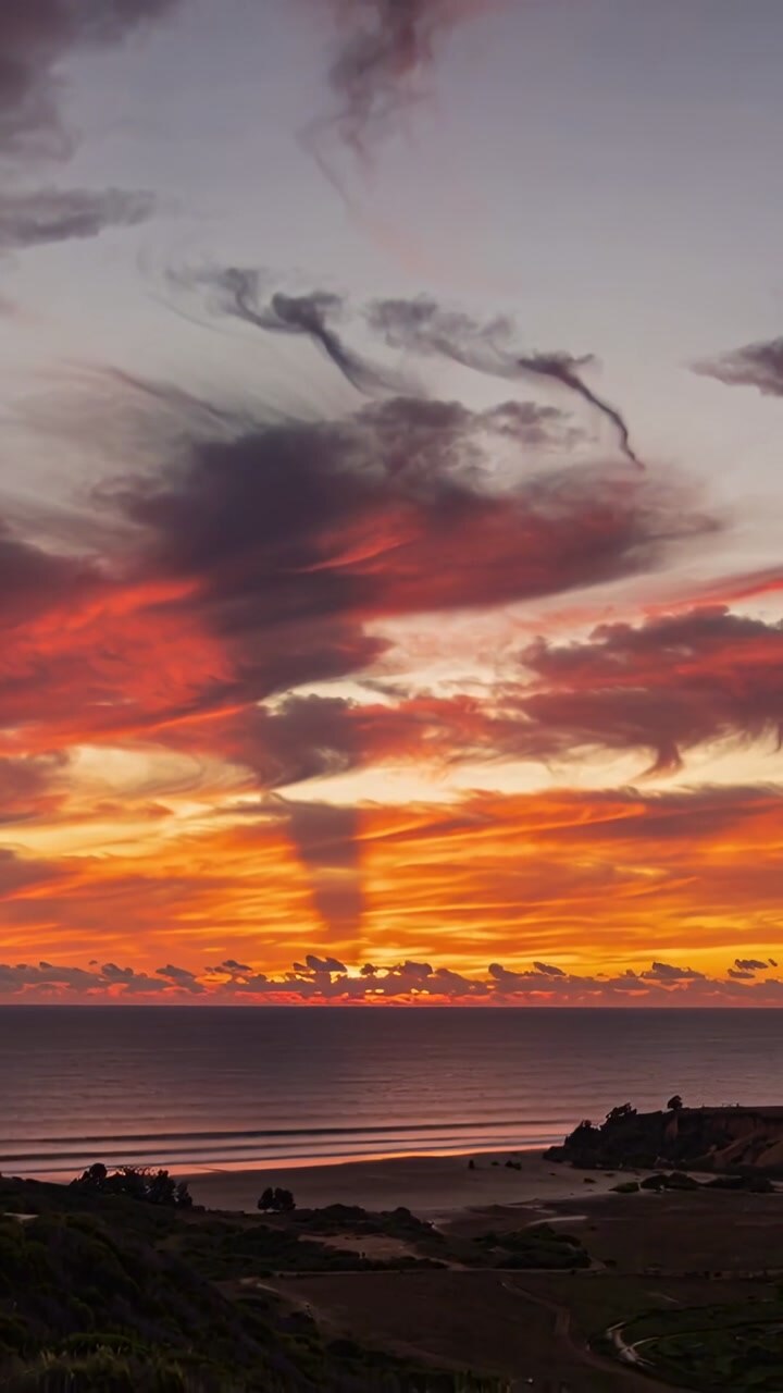 Vertical video: Showing sunset sky and clouds glowing as sun sinking below horizon by ocean