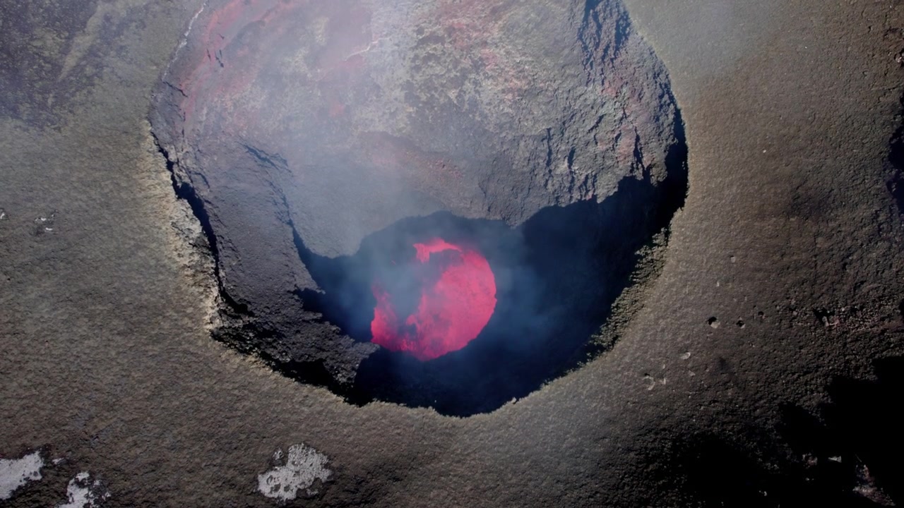 Vista aerea di una caldera vulcanica che rivela lava rosso vivo che ribolle sotto un sottile strato di fumo.