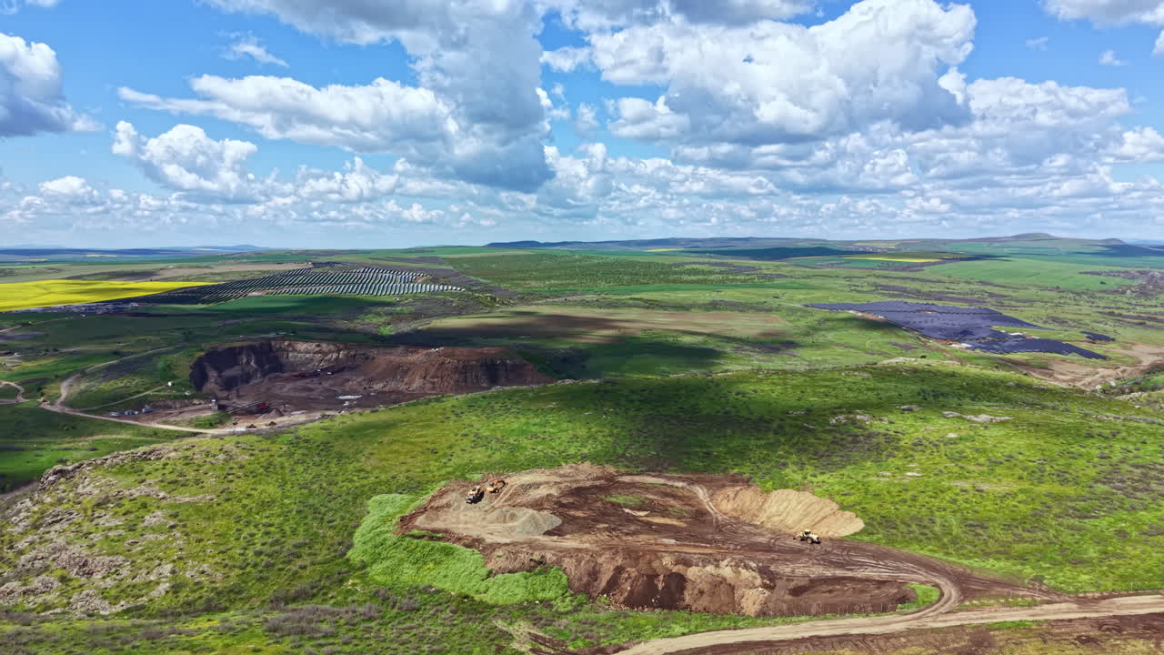 Painéis solares estão sendo instalados em um campo verde com nuvens e colinas ao fundo, sob um céu azul.