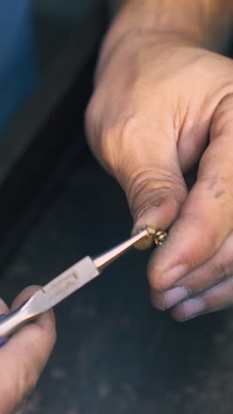 cu: skilled goldsmith connects little metal links to chain above dark wooden table in old jewelry workshop close view