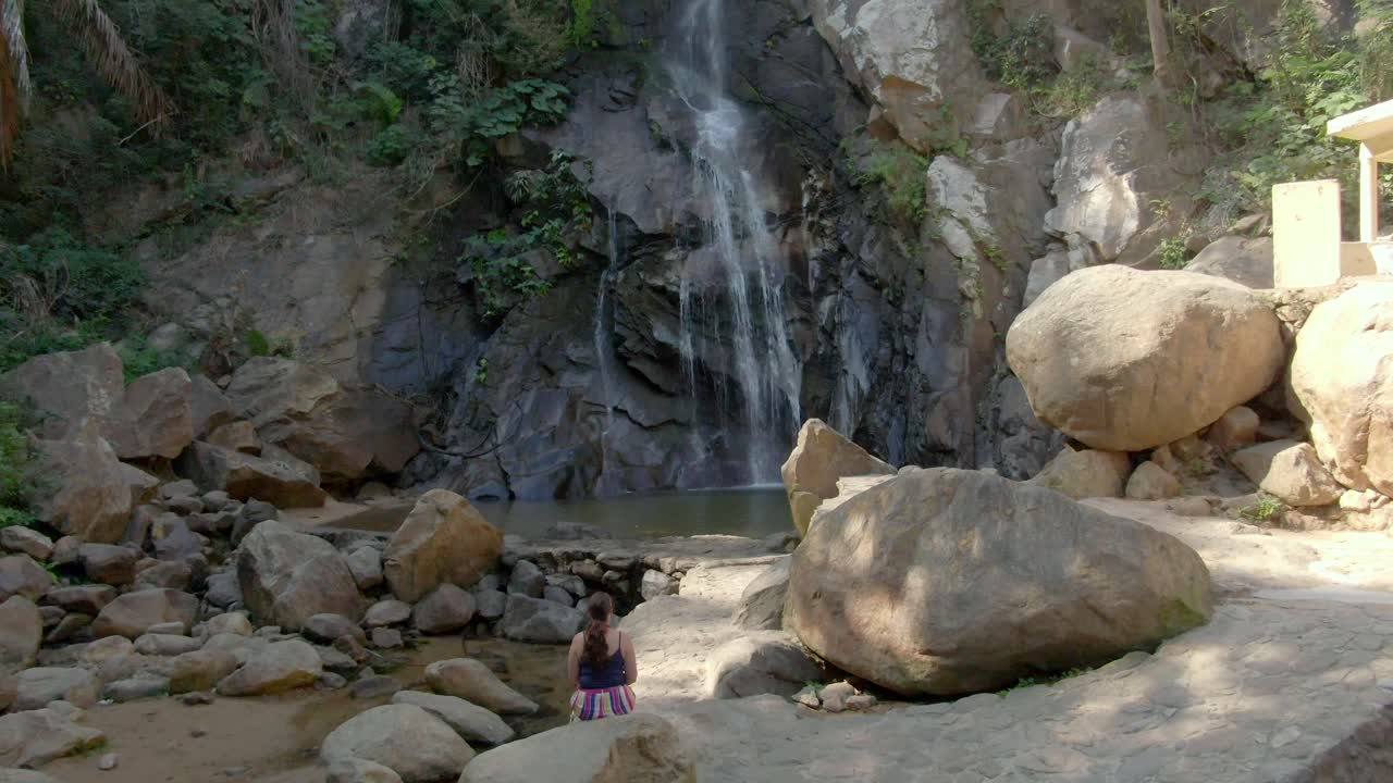 mujer sentada sola en la roca frente a la cascada de yelapa que desemboca en el río