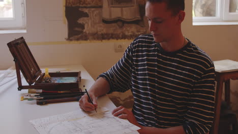 young man drawing sketch at table with wooden drawing set by his side