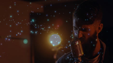 Bearded male singer performing on stage with mic, floating blue light particles in music production