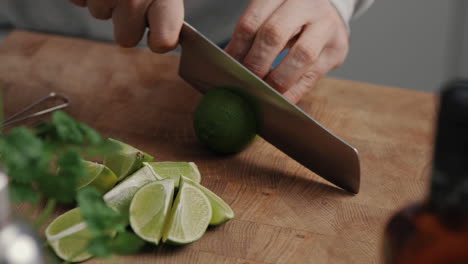 young male cutting a lime in half with sharp knife on wooden cutting board in kitchen at home