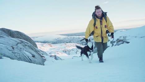 mountaineer together with alaskan malamute climb on snowy mountain at winter in norway