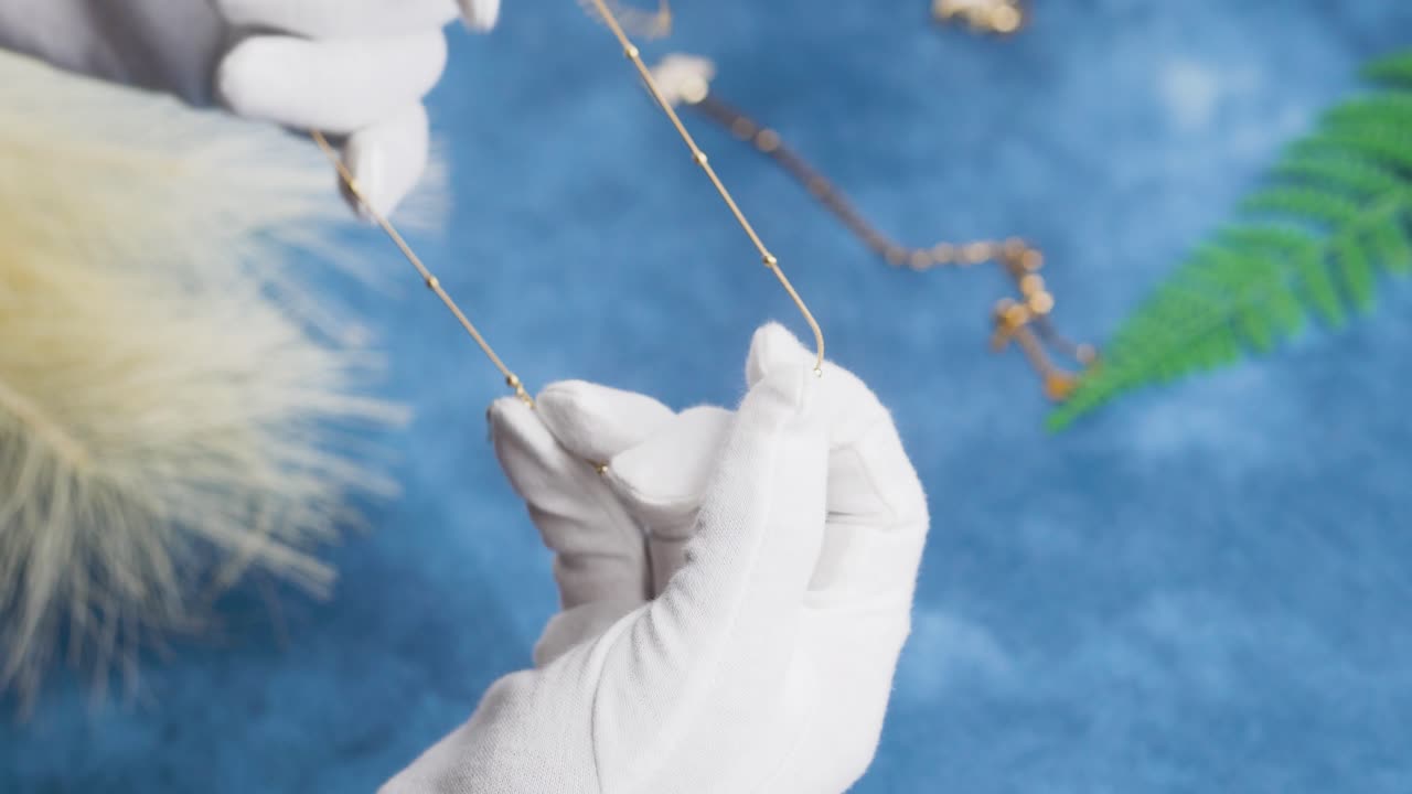 manos con guantes blancos sosteniendo y examinando joyas con una mesa de fondo azul