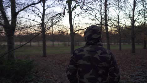 a man wearing a camouflage jacket in a slightly dark moody forest