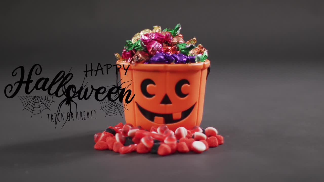 Happy halloween text banner with spider icon against pumpkin shaped bucket full of halloween candies