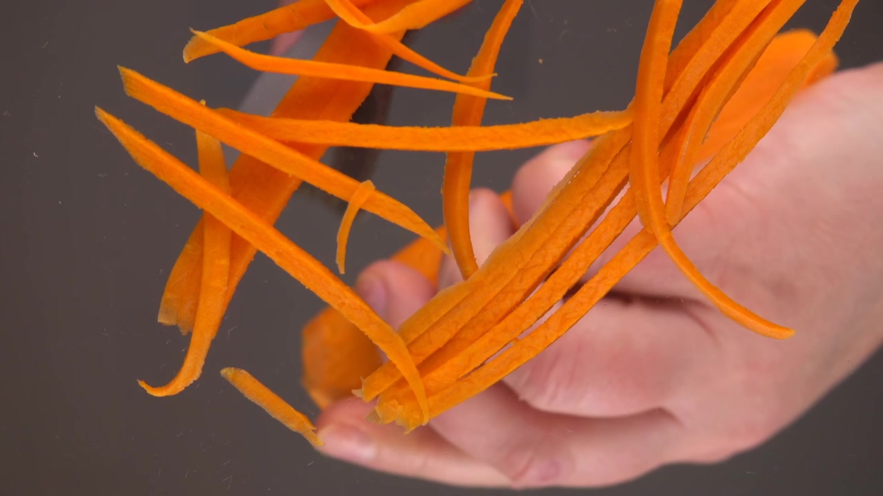 Slicing fresh carrots over a glass bowl. Bottom view.