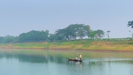 telephoto shot of fisherman stirring boat while woman is sitting down, sylhet